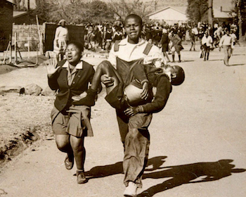 An image of three young black African students in the Soweto Uprsing, one of which is carrying a fallen student named Hector Pieterson, aged 13.